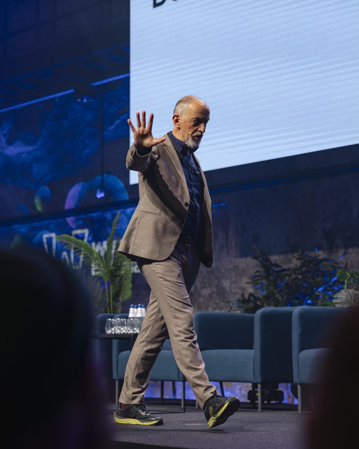 Steve Rawling on stage mid-talk, hand raised in a gesture, walking across a lit conference stage.